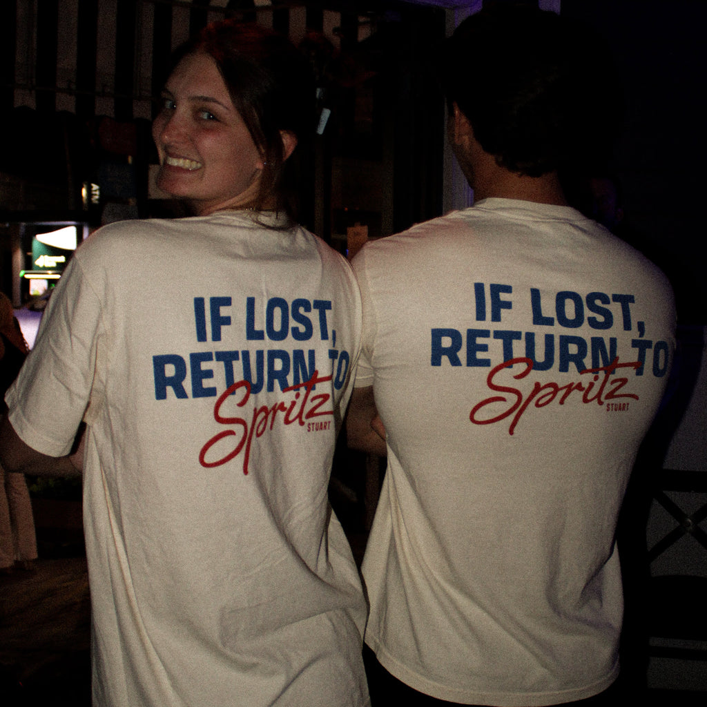 Two people wearing white t-shirts with text on the back, standing in a dark indoor setting.