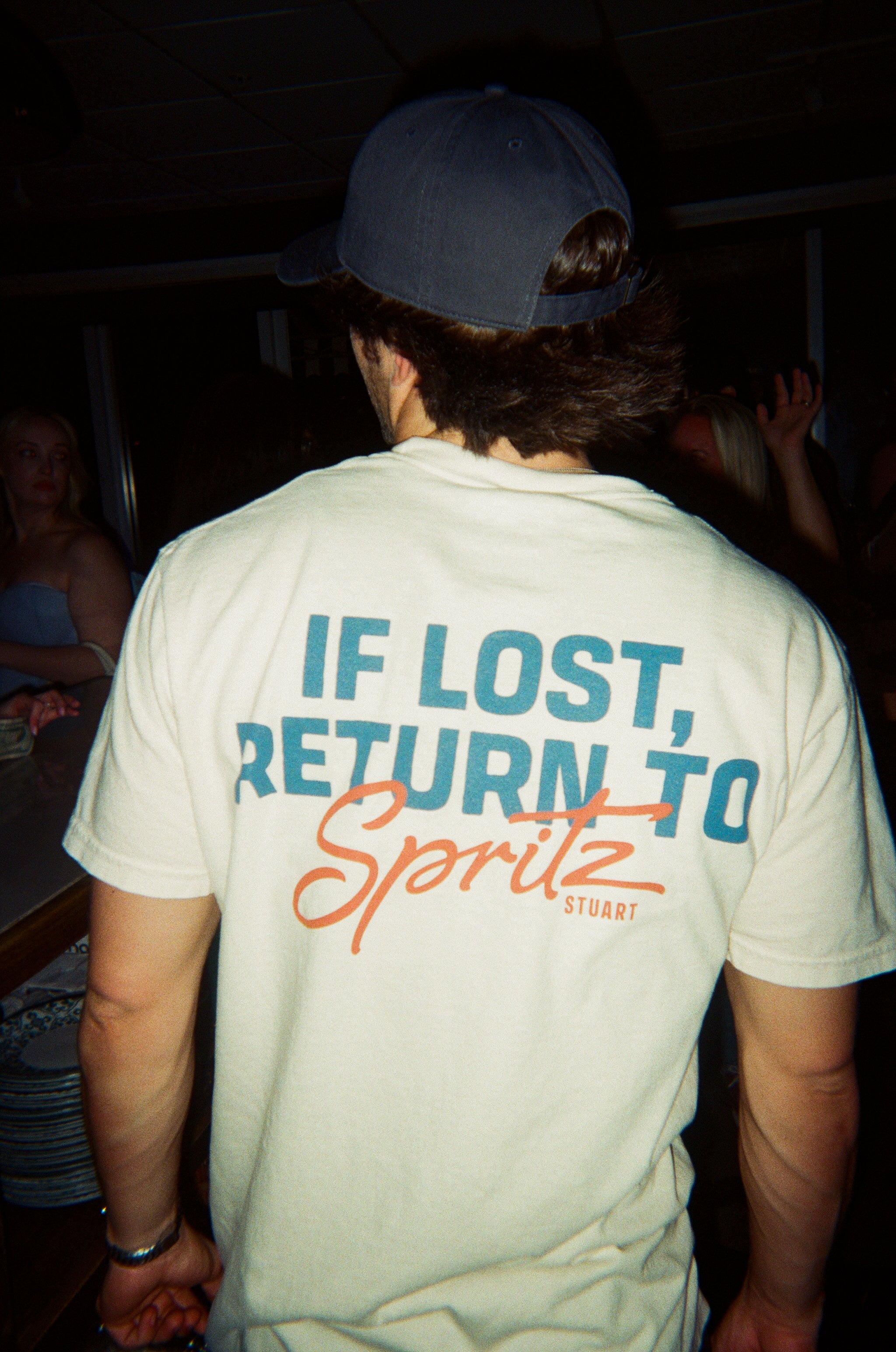 Person wearing a white t-shirt with 'If Lost, Return to Spritz Stuart' text.